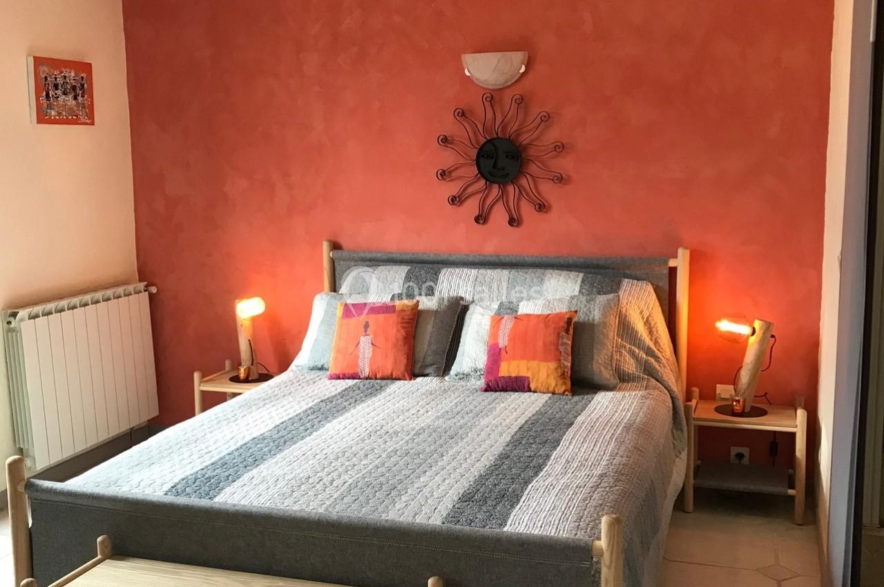 Chambre avec un lit double, mur orange, décoration murale en métal, lampes de chevet et coussins colorés.