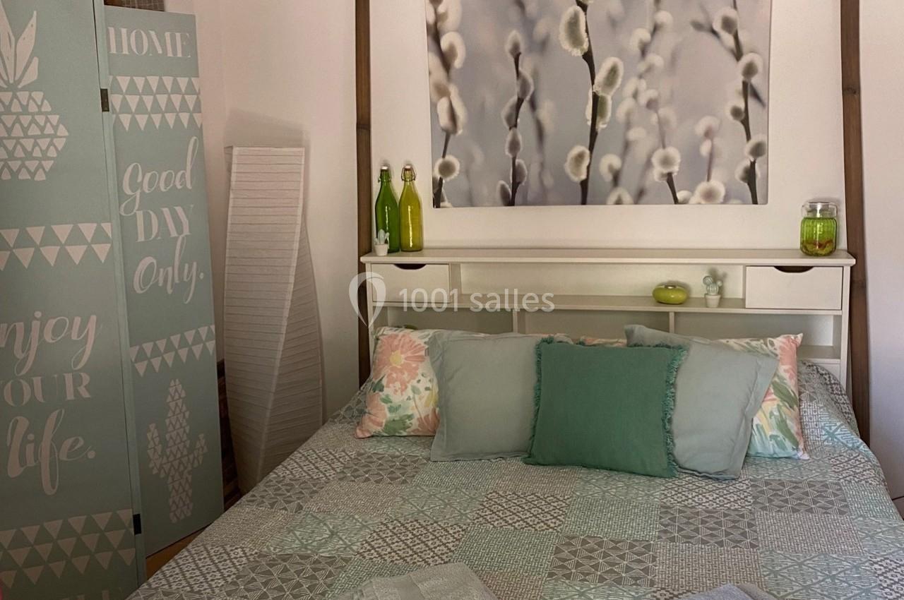 Chambre lumineuse avec lit aux tons pastel, tableau de chatons de saule, paravent décoratif et objets décoratifs assortis.