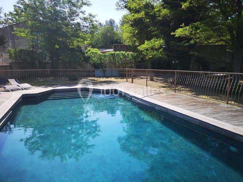 Piscine extérieure entourée de végétation, avec terrasse en bois et chaises longues à proximité.