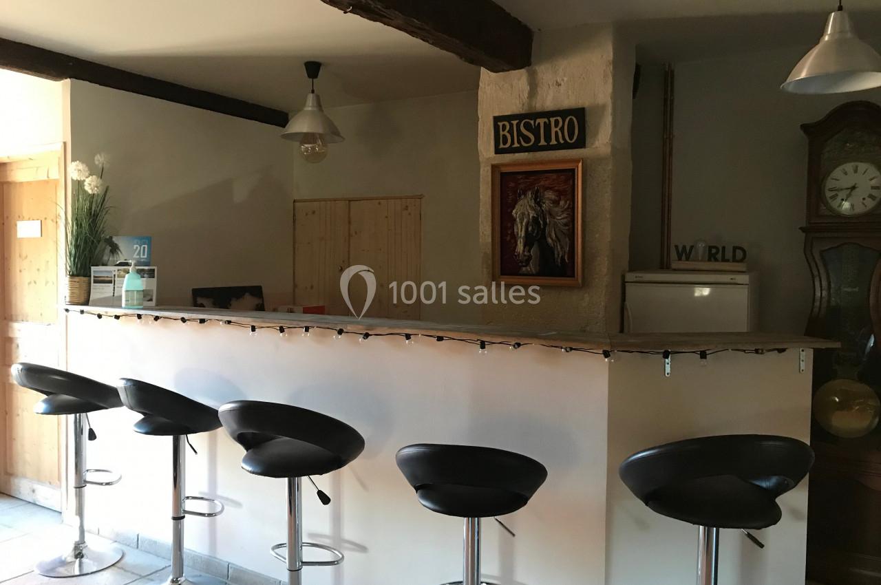 Comptoir de bar avec tabourets noirs, décoré de guirlandes lumineuses, dans une pièce au style rustique.