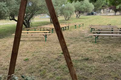 Structure en bois triangulaire devant des bancs disposés en plein air sur une pelouse entourée d'arbres.