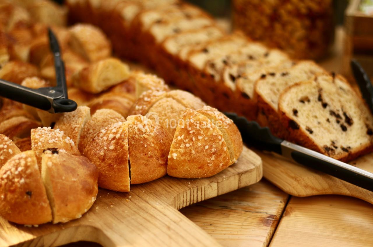 Assortiment de pains tranchés et viennoiseries disposés sur des planches en bois avec des pinces de service.