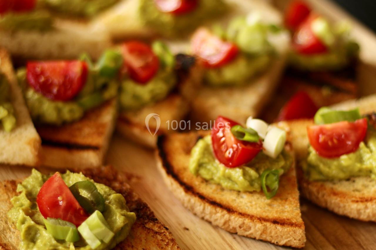 Tranches de pain grillé garnies de guacamole, de tomates cerises et de ciboulette sur une planche en bois.