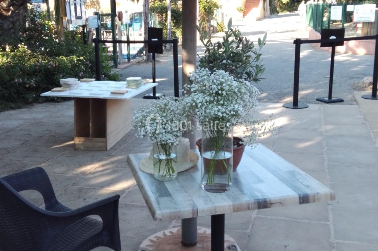 Table en marbre avec des bouquets de fleurs blanches sous un parasol en feuilles de palmier, dans un espace extérieur.