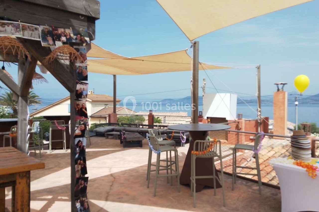 Terrasse ensoleillée avec des voiles d'ombrage, mobilier de jardin et vue sur la mer et les toits environnants.