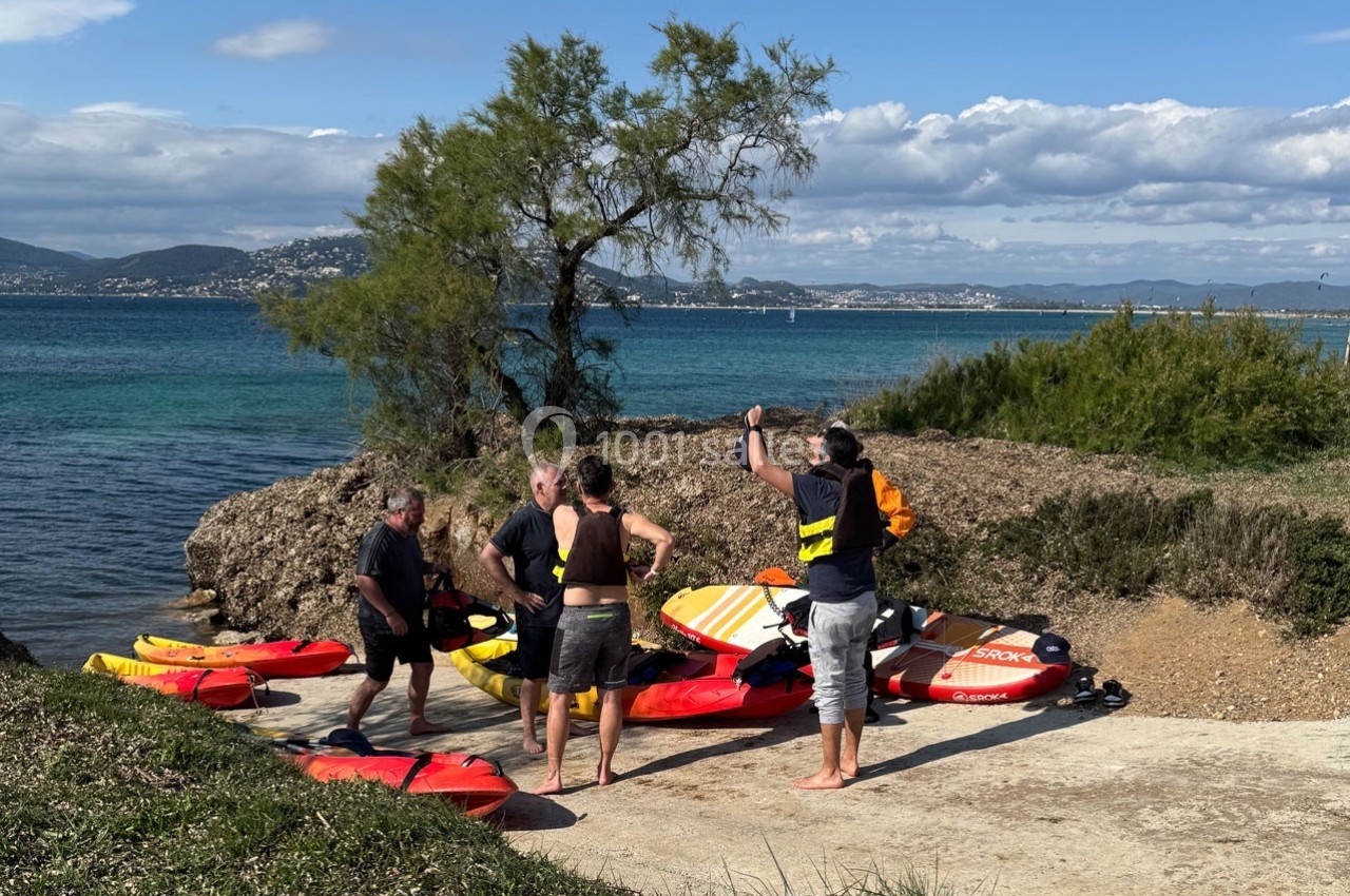 Un groupe de personnes prépare des planches de paddle sur une rampe près d'une étendue d'eau bordée de végétation.