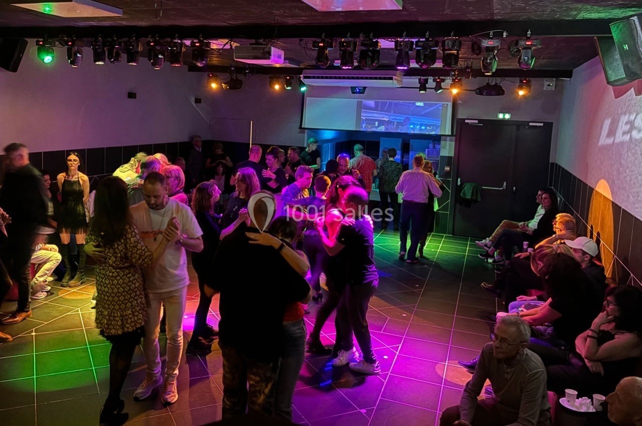 Des personnes dansent en couple sur une piste éclairée par des lumières colorées, tandis que d'autres sont assises autour.