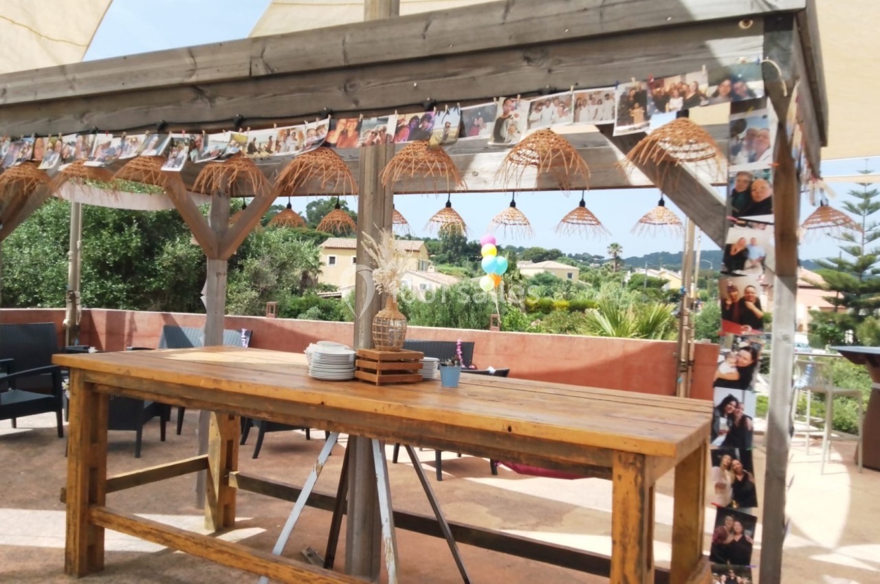 Pergola en bois décorée de guirlandes de photos et de lampes suspendues, avec une table en bois au premier plan.