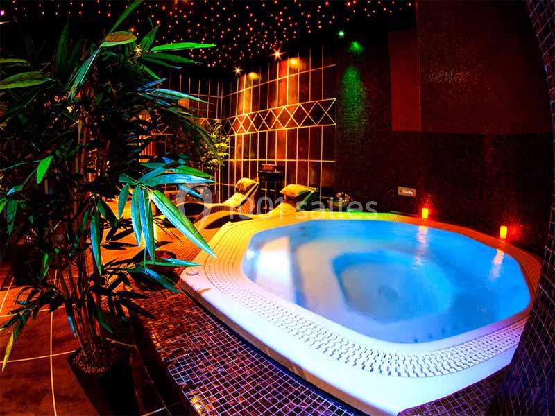 Jacuzzi éclairé dans une pièce sombre avec des plantes, des chaises longues et un plafond étoilé.