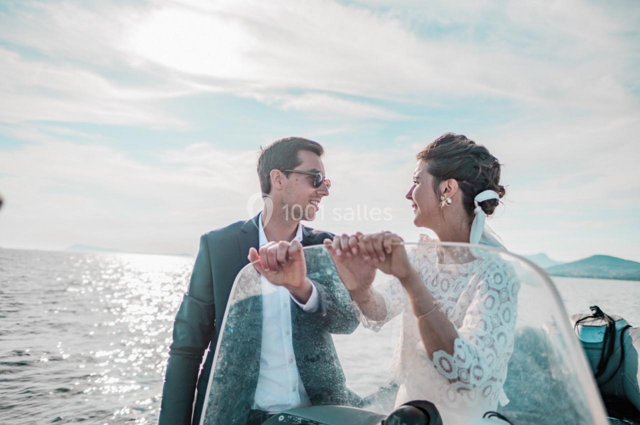 Un couple souriant sur un bateau, naviguant sur une mer calme sous un ciel partiellement nuageux.