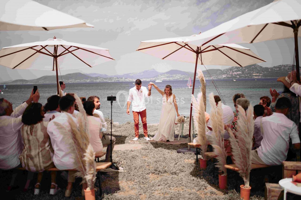 Un couple se tenant la main lors d'une cérémonie de mariage en plein air, près de la mer, sous des parasols.