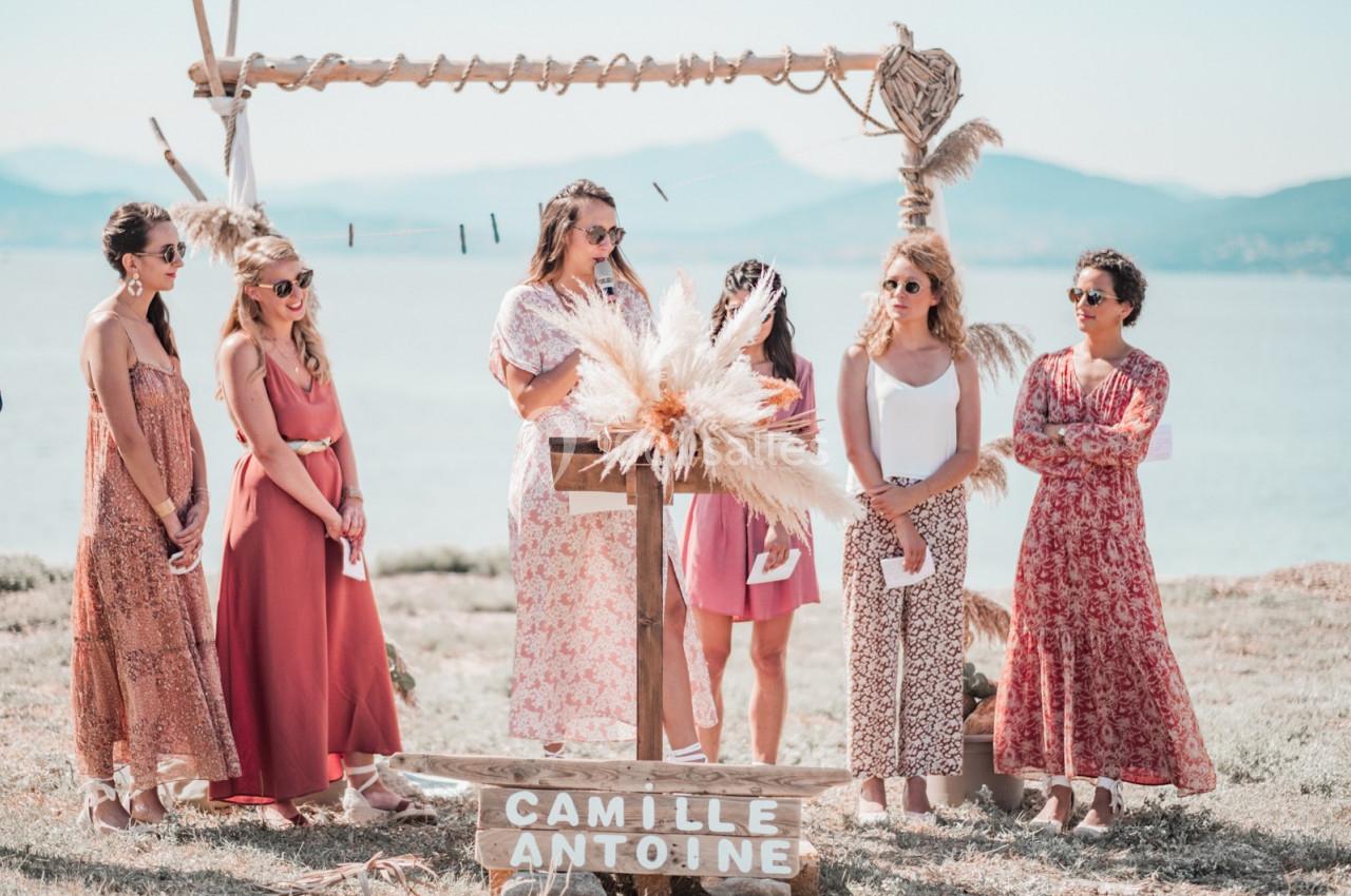 Cérémonie en plein air avec plusieurs femmes autour d'un pupitre décoré de pampas, près d'un lac ou de la mer.