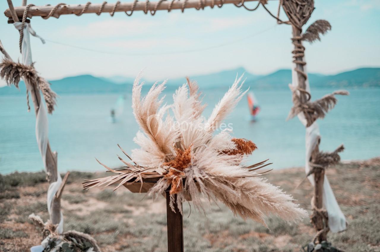Arrangement de fleurs séchées devant une arche en bois décorée, avec vue sur un lac et des montagnes en arrière-plan.