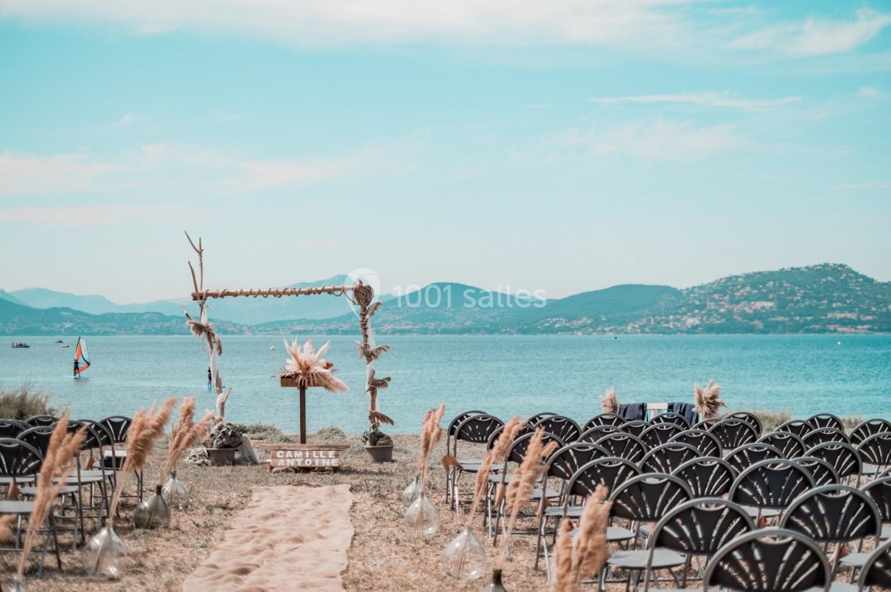 Chaises disposées face à une arche décorée en bord de mer, avec vue sur des collines et un ciel dégagé.