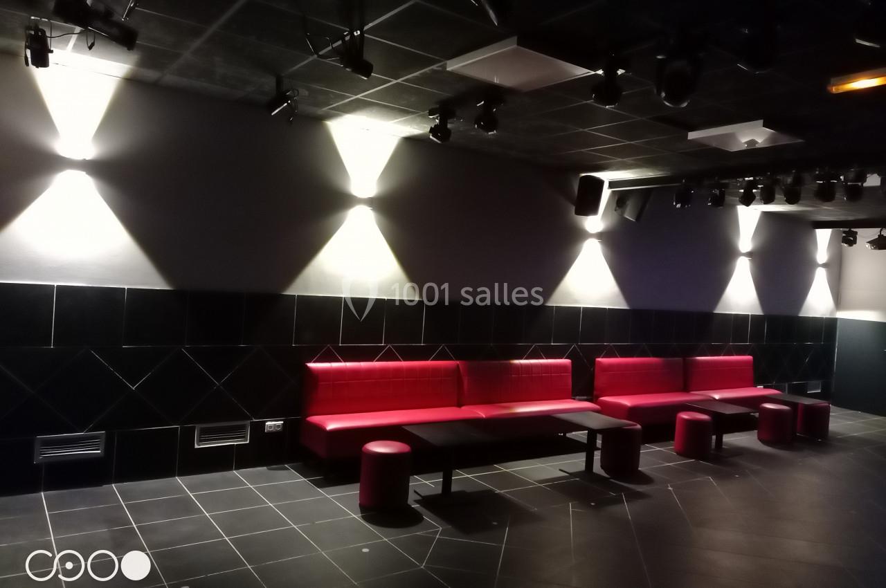 Salle sombre avec des banquettes rouges, des tabourets assortis et un éclairage mural diffus.