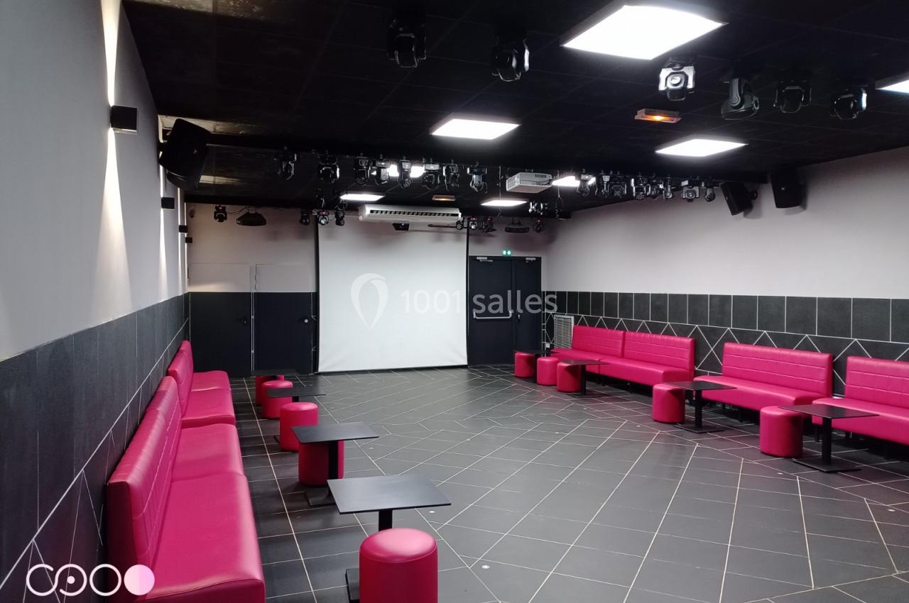 Salle moderne avec banquettes rouges, tables noires, sol carrelé sombre et écran blanc au fond.