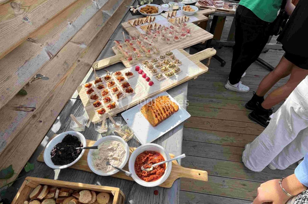 Buffet en extérieur avec divers amuse-bouches, tartinades, pain et condiments disposés sur des planches en bois.