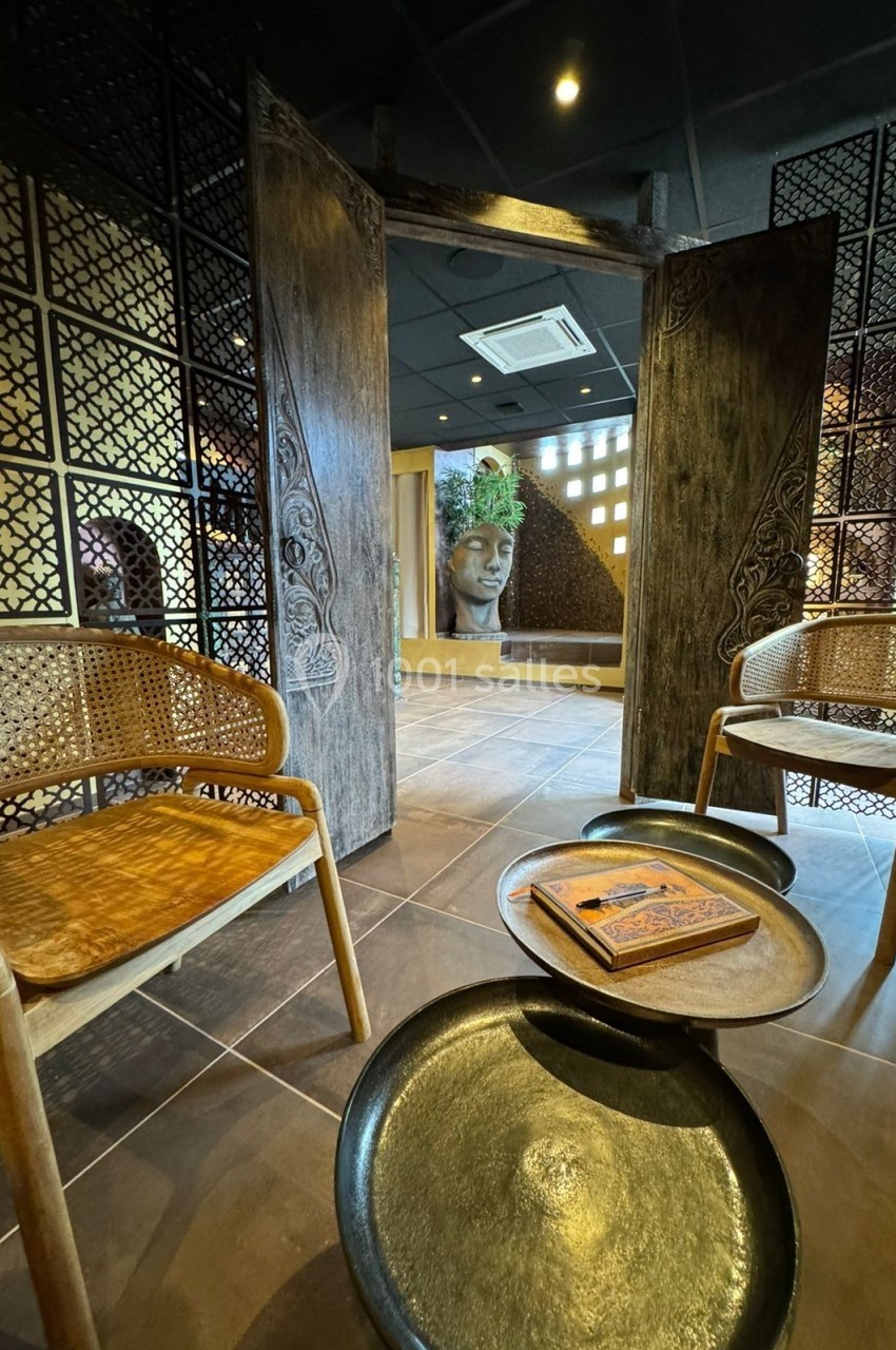 Deux fauteuils en rotin entourent une table basse avec un livre, dans un espace décoré de motifs asiatiques et une statue…