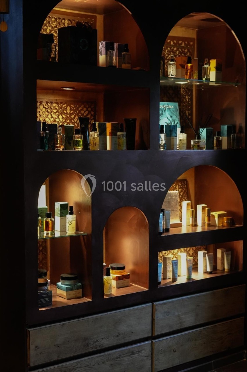 Étagères éclairées contenant des flacons de parfum et des produits cosmétiques dans un décor sombre et élégant.