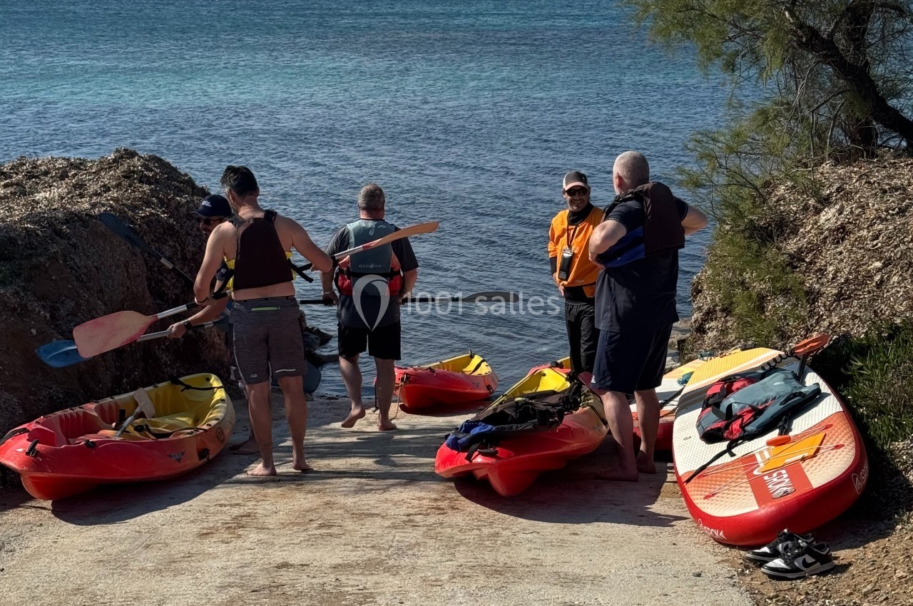 Des personnes préparent des kayaks sur une rampe en bord de mer, avec une vue sur des collines à l'horizon.