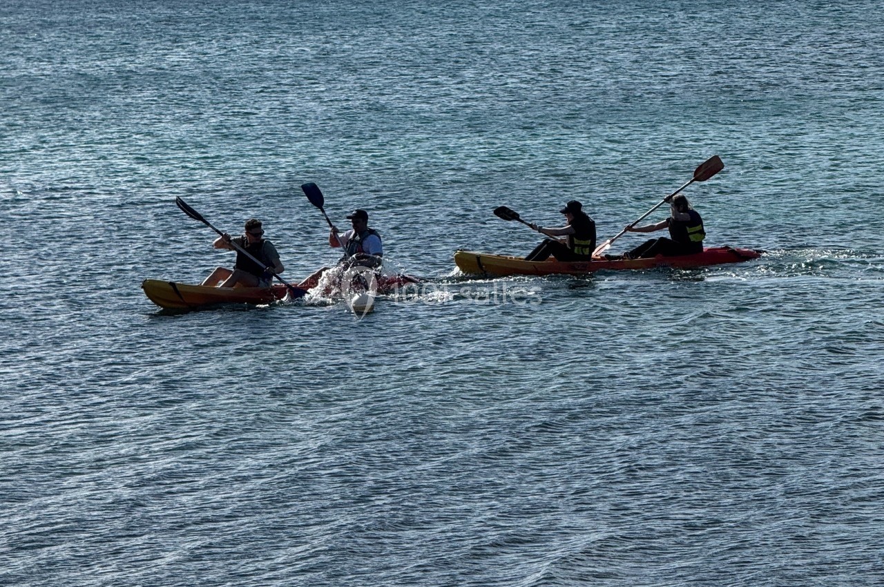 Quatre personnes pagayant sur deux kayaks doubles dans une mer calme, avec des îles en arrière-plan.