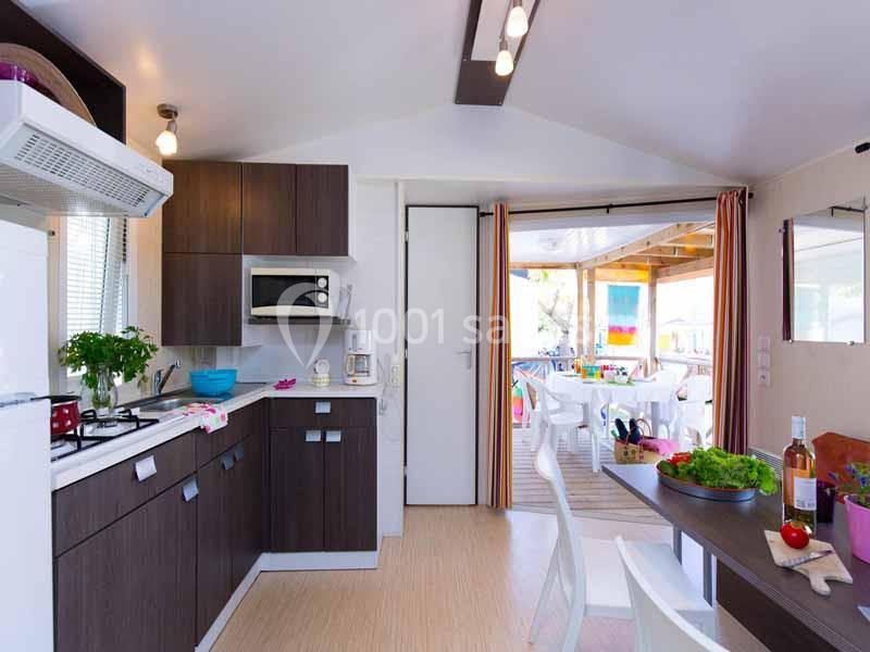 Cuisine moderne avec meubles en bois sombre, table dressée, et vue sur une terrasse lumineuse aménagée.