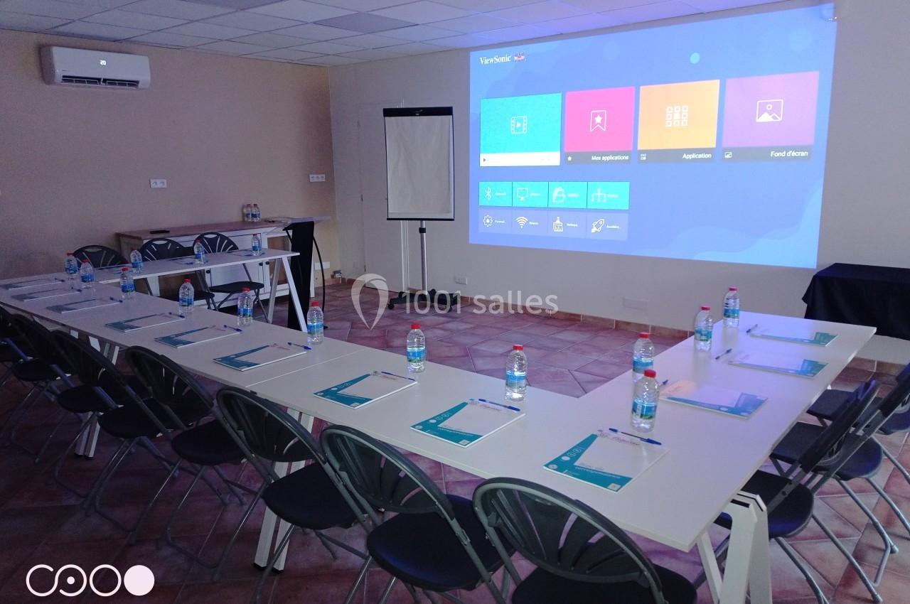 Salle de réunion équipée avec tables en U, chaises, écran de projection, paperboard et documents disposés sur les tables.