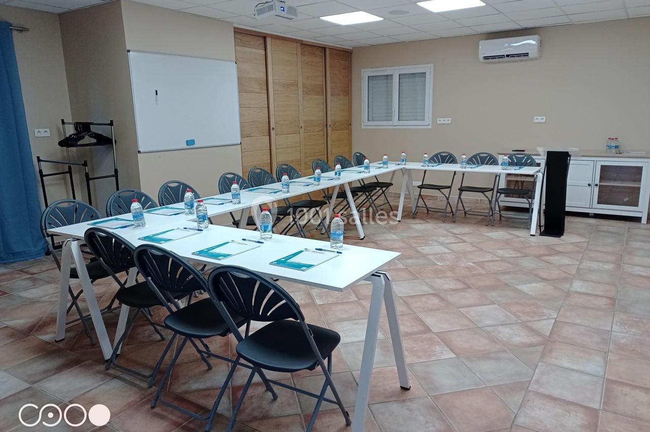 Salle de réunion équipée de tables disposées en U, chaises, bouteilles d'eau, paperboards et écran de projection.
