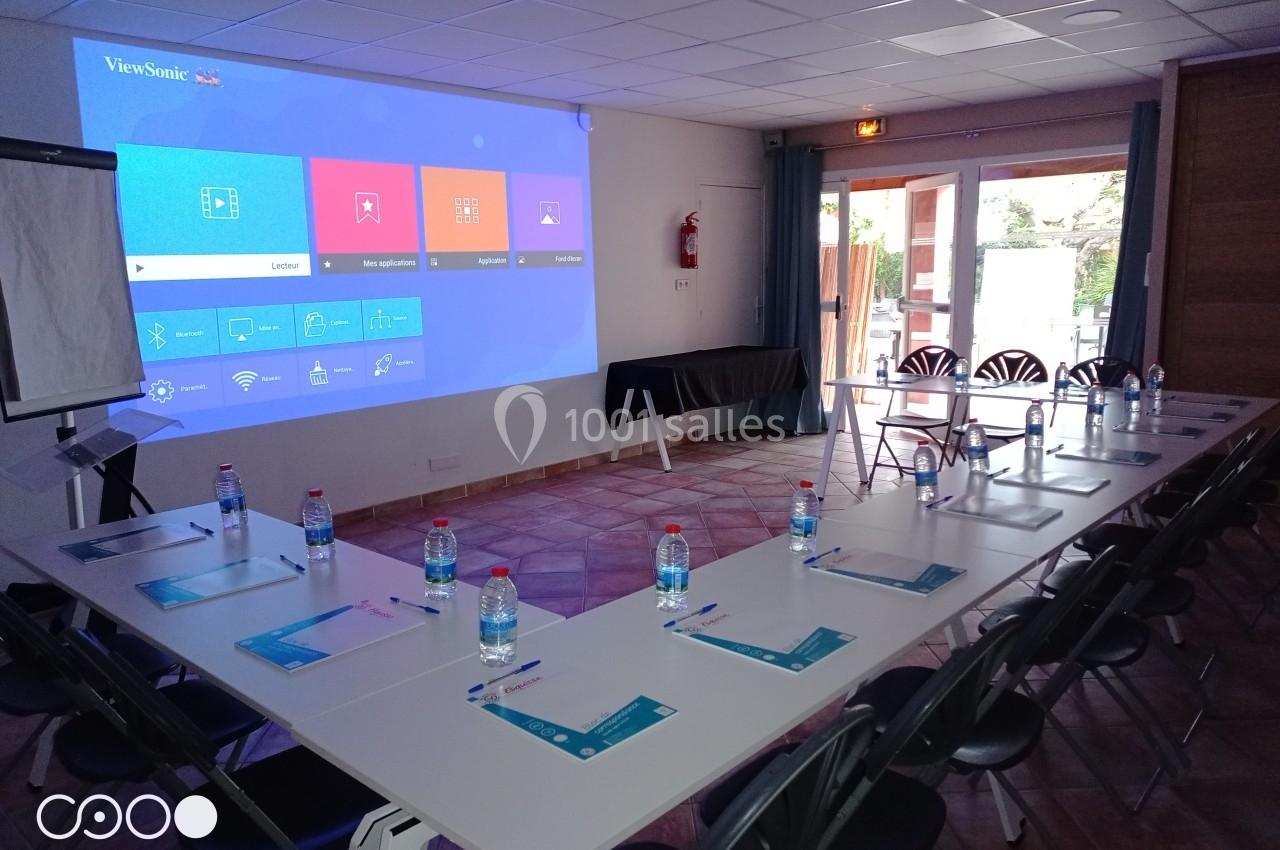 Salle de réunion équipée d'un projecteur affichant un écran d'accueil, tables disposées en U avec documents et bouteilles d…