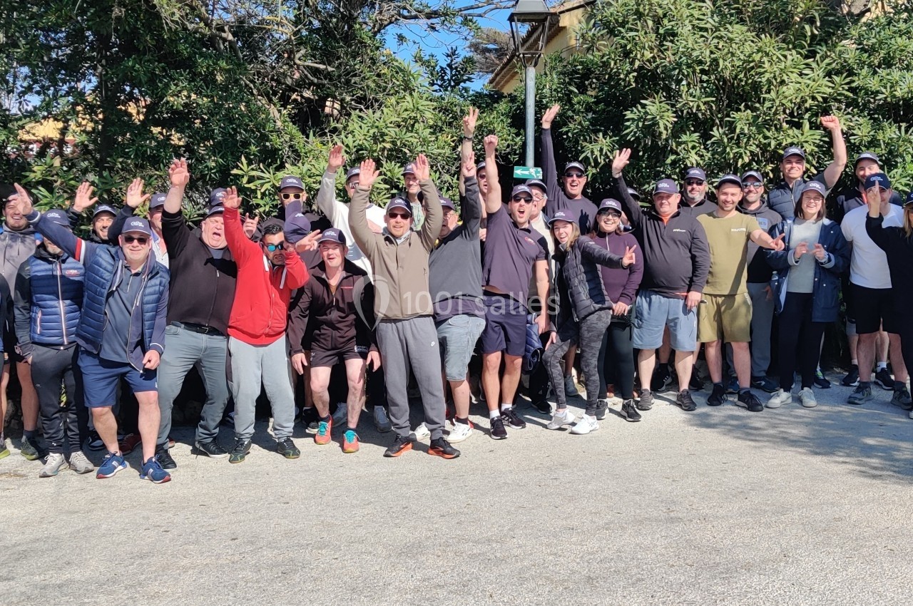 Un groupe de personnes souriantes levant les bras, rassemblées en extérieur devant des arbres et des buissons.