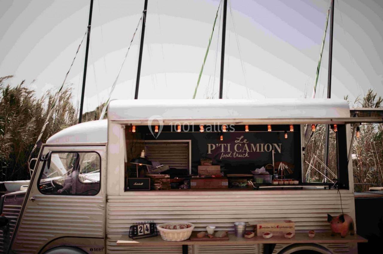 Food truck vintage stationné devant des roseaux et des mâts de bateau, avec une enseigne ’Le P'ti Camion’.