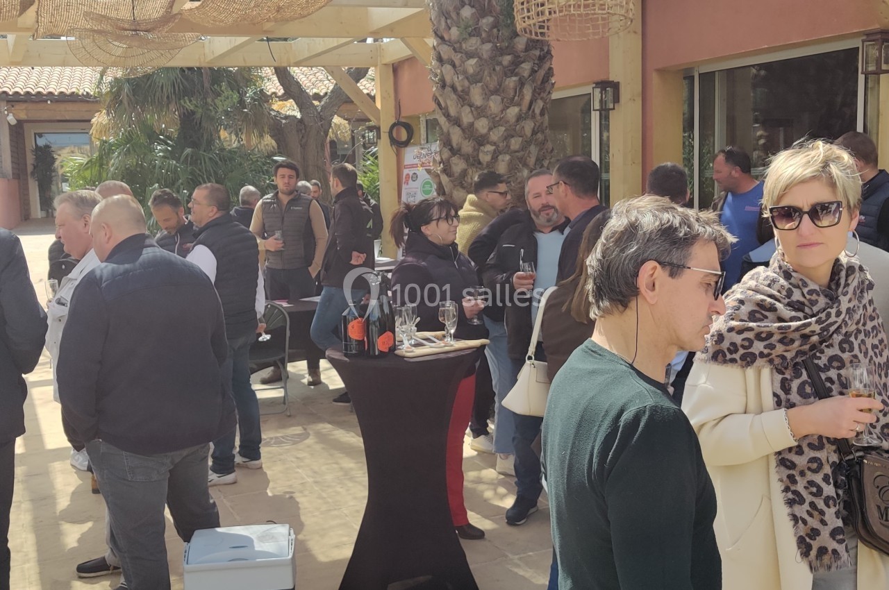 Un groupe de personnes discute en extérieur sous une pergola, avec des tables et des décorations en osier.