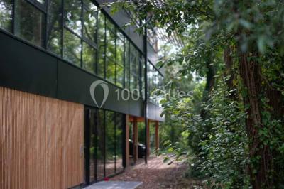 Salle de réunion lumineuse avec table en bois, quatre chaises noires, écran mural et cloison vitrée donnant sur l'extérieur.