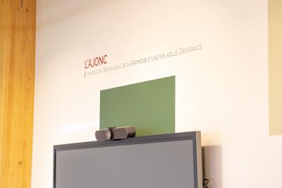 Salle de réunion lumineuse avec table en bois, quatre chaises noires, écran mural et cloison vitrée donnant sur l'extérieur.