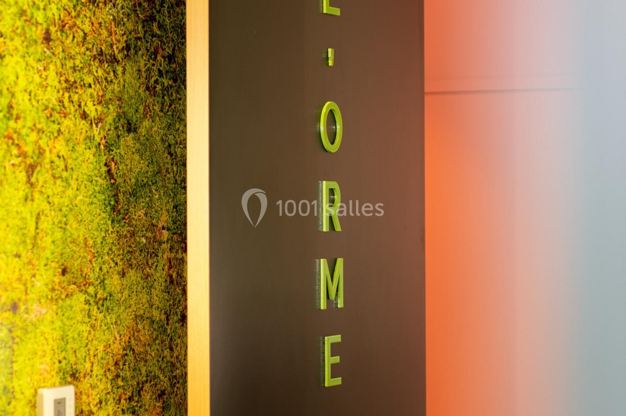 Porte noire entrouverte avec l'inscription ’L'ORME’ en lettres vertes, mur végétal en arrière-plan.