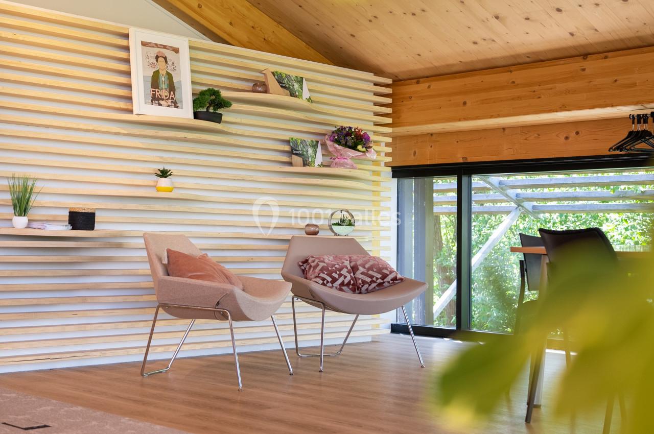 Espace intérieur lumineux avec mur en bois à étagères, fauteuils modernes et vue sur la végétation extérieure.