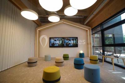 Salle de réunion lumineuse avec table en bois, quatre chaises noires, écran mural et cloison vitrée donnant sur l'extérieur.
