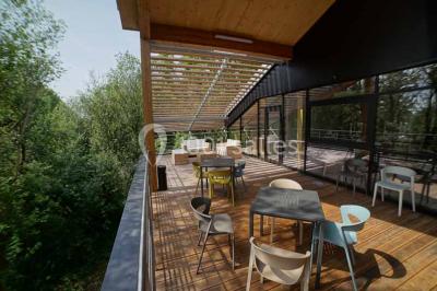 Salle de réunion lumineuse avec table en bois, quatre chaises noires, écran mural et cloison vitrée donnant sur l'extérieur.