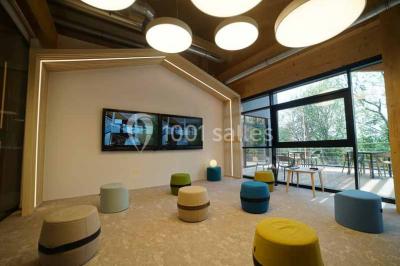 Salle de réunion lumineuse avec table en bois, quatre chaises noires, écran mural et cloison vitrée donnant sur l'extérieur.