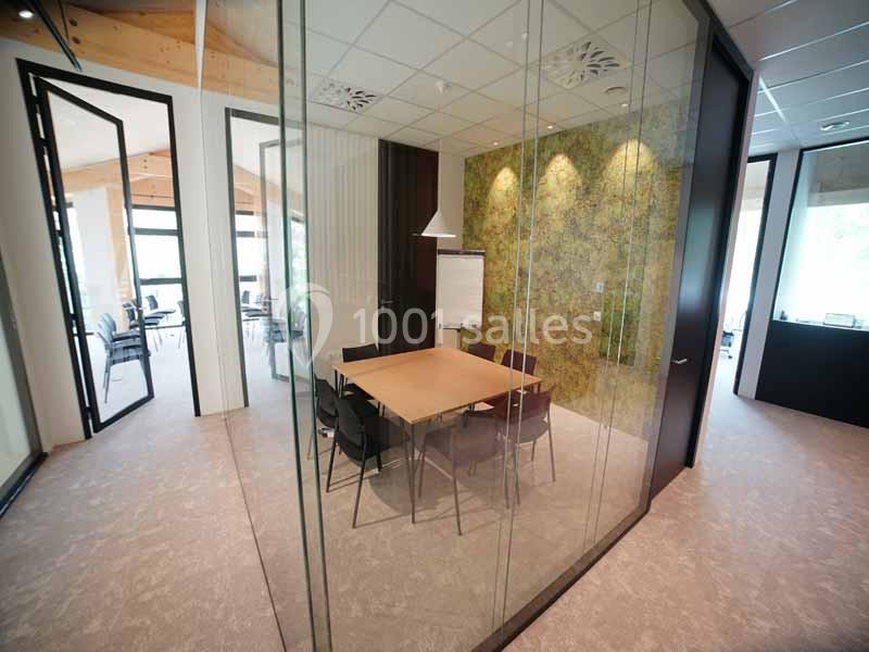 Salle de réunion vitrée avec table en bois, chaises noires, tableau blanc et mur végétal en arrière-plan.