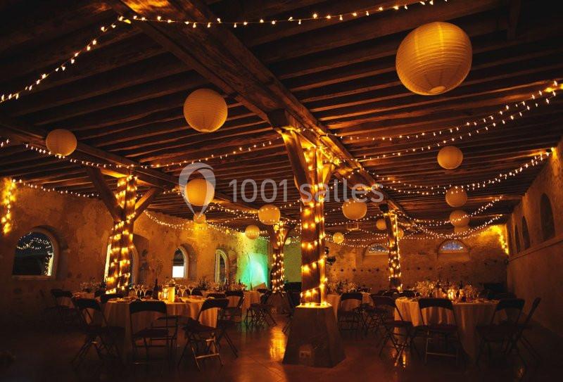 Salle de réception décorée avec des guirlandes lumineuses et des lanternes suspendues, ambiance chaleureuse et festive.