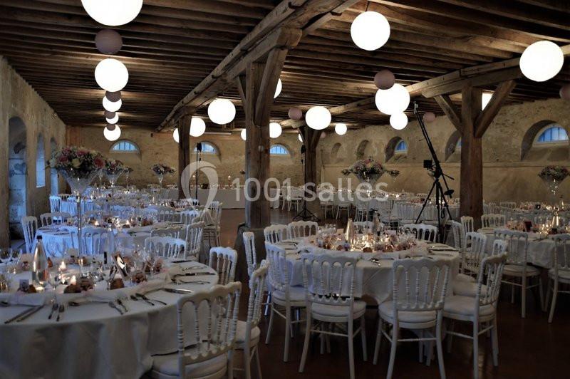 Salle de réception décorée avec des tables rondes, chaises blanches, éclairage doux et arrangements floraux.