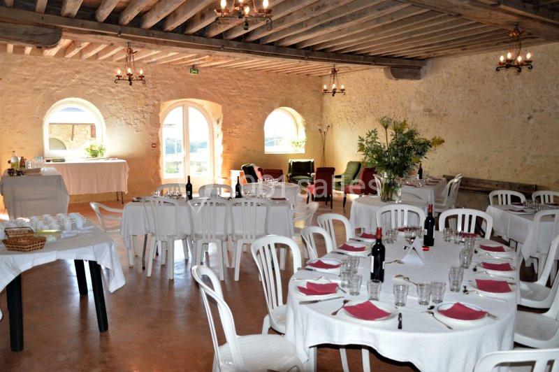 Salle de réception lumineuse avec tables dressées, chaises blanches, nappes blanches et décorations florales.