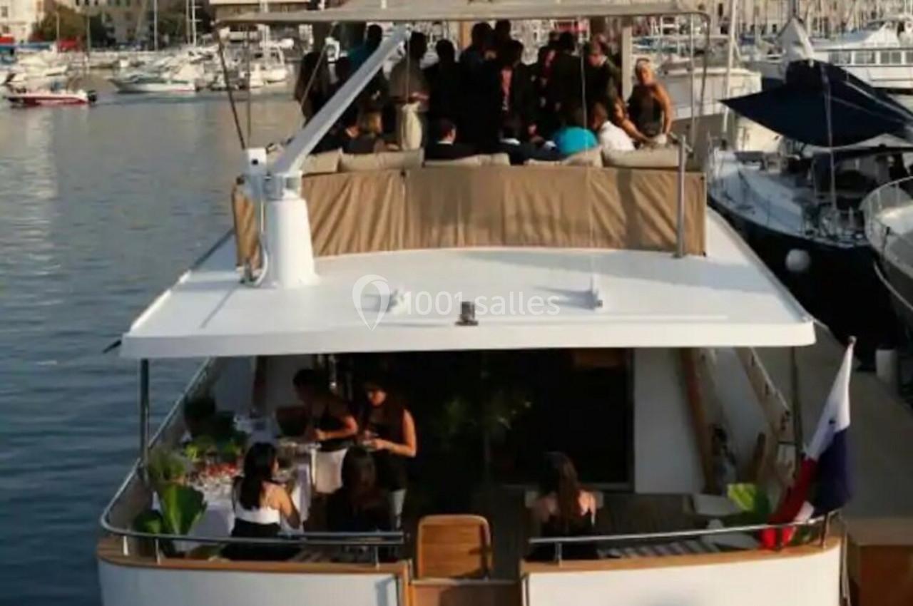 Vue arrière d'un yacht amarré dans un port, avec des personnes rassemblées sur le pont supérieur.