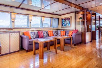 Un bateau à moteur tracte une bouée gonflable sur une mer calme, avec un yacht et une côte boisée en arrière-plan.