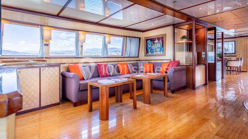 Salon spacieux avec canapé violet, coussins colorés, tables en bois et grandes fenêtres offrant une vue sur l'extérieur.