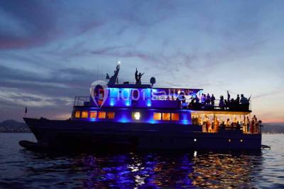 Un bateau à moteur tracte une bouée gonflable sur une mer calme, avec un yacht et une côte boisée en arrière-plan.