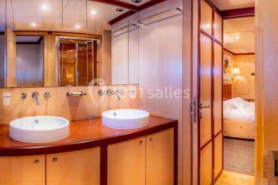 Un bateau à moteur tracte une bouée gonflable sur une mer calme, avec un yacht et une côte boisée en arrière-plan.