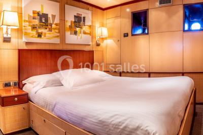 Un bateau à moteur tracte une bouée gonflable sur une mer calme, avec un yacht et une côte boisée en arrière-plan.