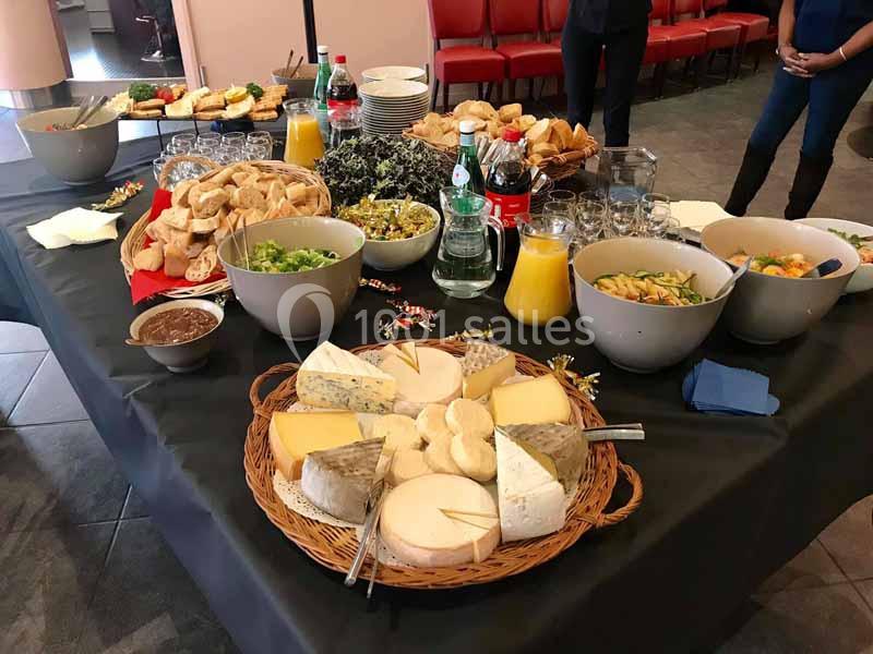 Table garnie de fromages, salades, pains, boissons et condiments, disposée pour un buffet.